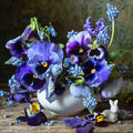 A fine art print with floral still life featuring deep blue pansies, muscari, and forget-me-nots in a vintage white porcelain bowl, set against a textured background with a porcelain bunny figurine.
