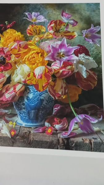 A rich still life composition of vibrant Parrot and Rembrandt tulips in shades of gold, red, white, and lilac, arranged in an antique blue-and-white vase. The petals have dramatic ruffled edges and painterly streaks, with fallen blossoms scattered on a rustic wooden table.